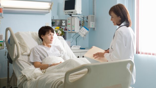 alt="Female doctor talking to female patient lying in hospital bed"