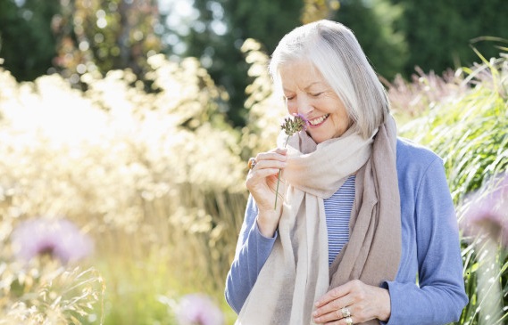 alt="Older woman smelling flowers outdoors"