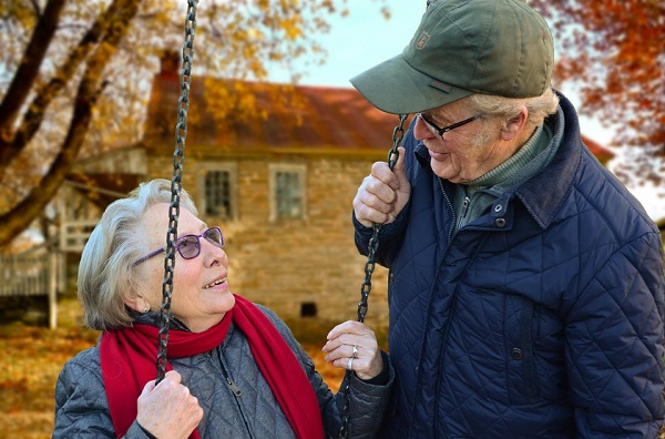 Older man standing next to his wife who is sitting in a swing